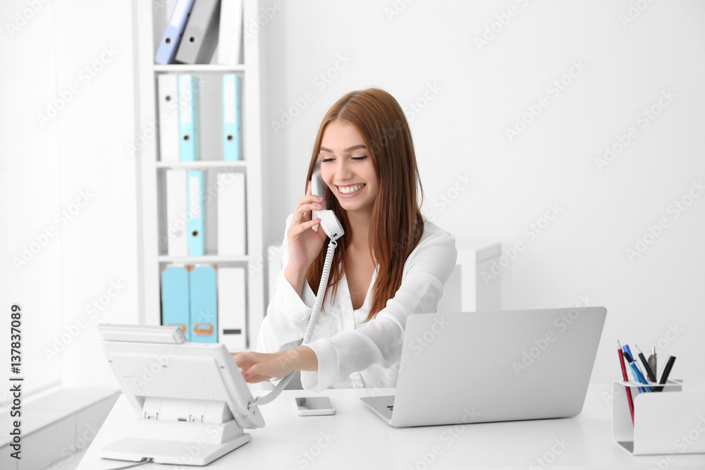 Young businesswoman sitting at office table and speaking by phone Young businesswoman sitting at office table and speaking by phone