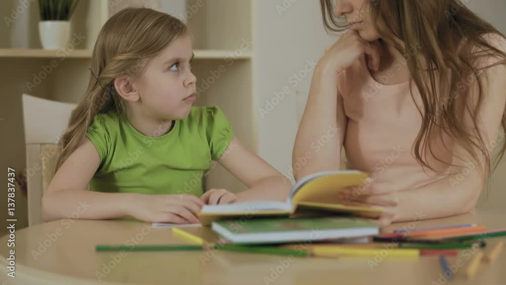 Upset little girl doing school tasks with mother, bored or tired of homework Upset little girl doing school tasks with mother, bored or tired of homework