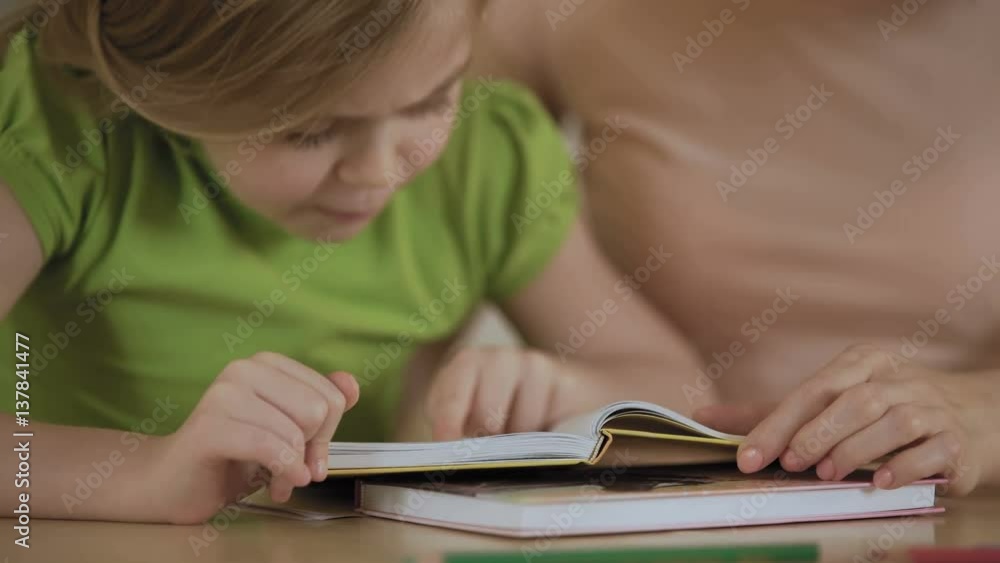 Smart little girl focused on reading funny story in book, smiling to mother Smart little girl focused on reading funny story in book, smiling to mother