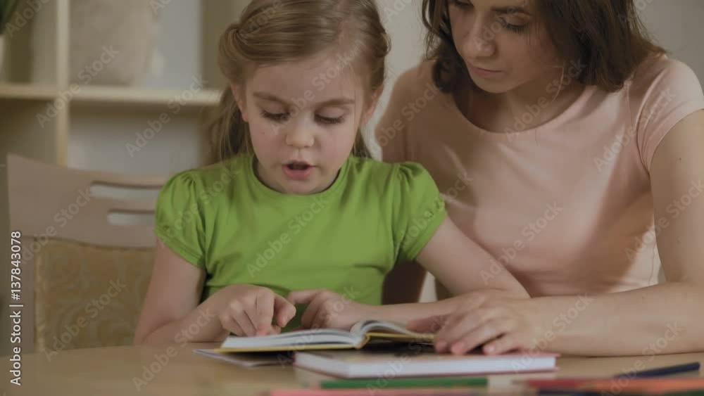 Girl reading interesting storybook for mother, woman proud of smart daughter Girl reading interesting storybook for mother, woman proud of smart daughter