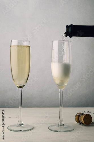 Pair of Fluted Champagne Glasses Being Filled on Wood Plank Table