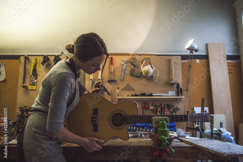 woman luthier is repairing a guitar in her musical instrument workshop photo