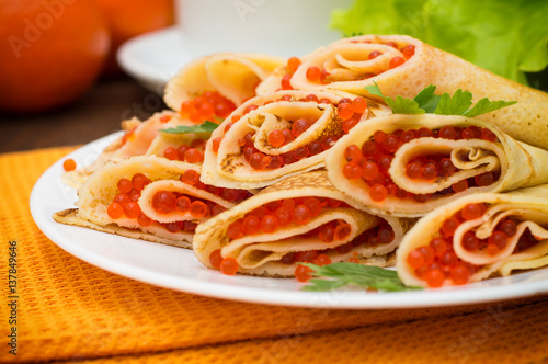 Rolls pancakes with red caviar. Russian cuisine. Flat lay. Maslenitsa. Wooden background. Close-up