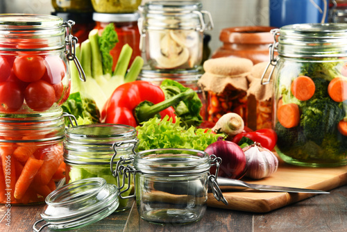 Jars with marinated food and raw vegetables on cutting board