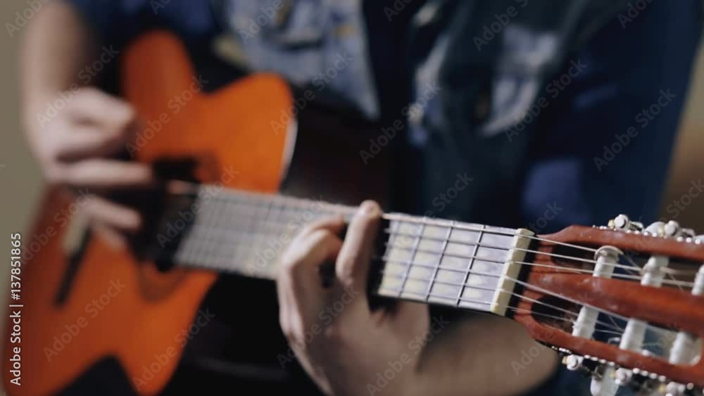 Closeup of guitarist playing on acoustic guitar sitting at gray wall background Closeup of guitarist playing on acoustic guitar sitting at gray wall background