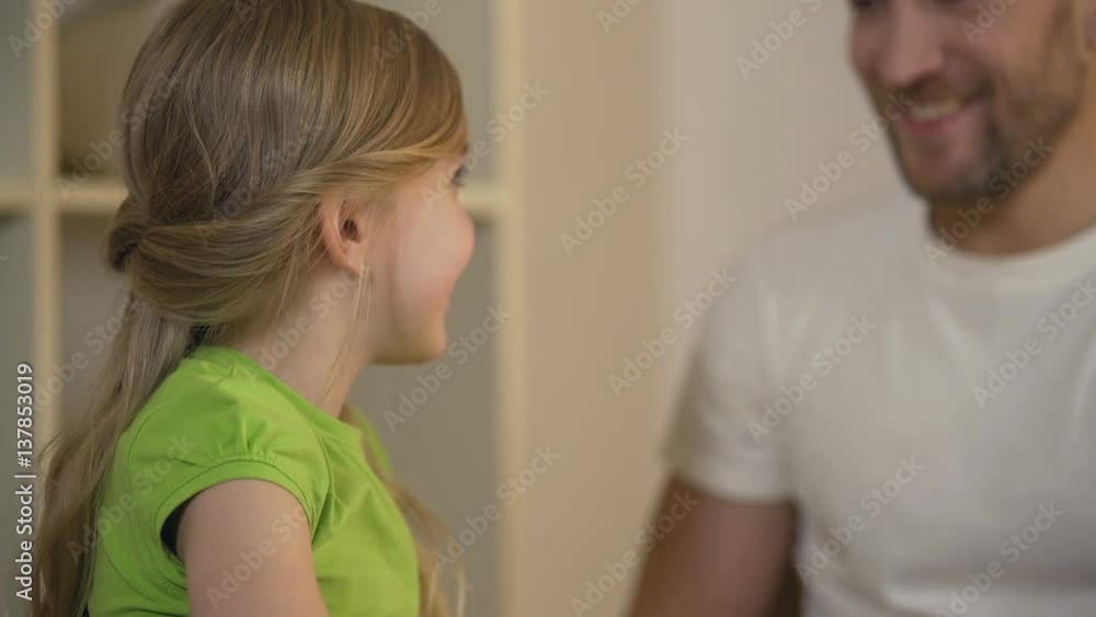 Cheerful daughter giving high five to smiling father, celebrating achievement Cheerful daughter giving high five to smiling father, celebrating achievement