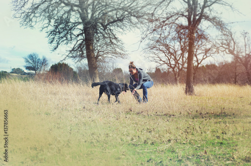 Female playing with black dog in sunny rural pasture. Feelings of fun and happiness.