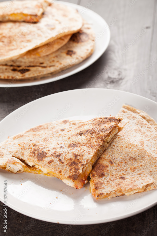 Crispy Quesadilla with Chicken and Sauce on white plate on dark wooden background vertical shot