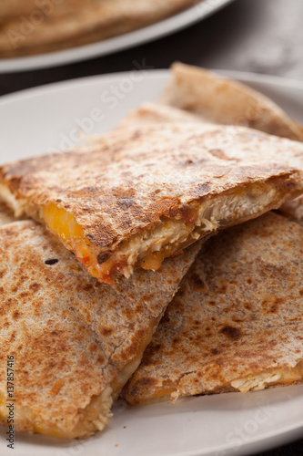 Crispy Quesadilla with Chicken and Sauce on white plate on dark wooden background stacked close up shot