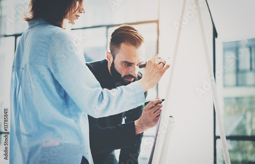 Teamwork and brainstorming concept.Young creative coworkers working with new startup project in modern office.Two colleagues writing on the presentation board.Horizontal,blurred background effect.