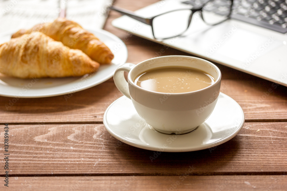 Business lunch with croissant and laptop on wooden desk Business lunch with croissant and laptop on wooden desk
