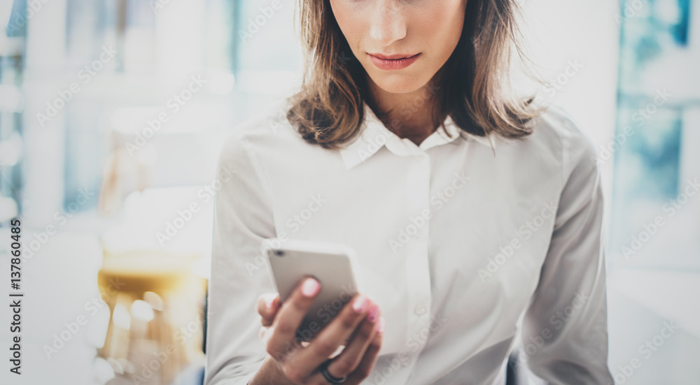 Portrait young business woman wearing white shirt using modern smartphone hands.Girl reading sms message in working process at sunny office.Panoramic windows background.Horizontal blurred.