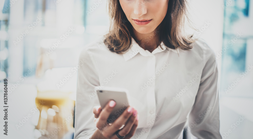 Portrait young business woman wearing white shirt using modern smartphone hands.Girl reading sms message in working process at sunny office.Panoramic windows background.Horizontal blurred. Portrait young business woman wearing white shirt using modern smartphone hands.Girl reading sms message in working process at sunny office.Panoramic windows background.Horizontal blurred.