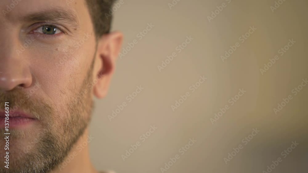 Half face of young man looking seriously at camera, male employment statistics Half face of young man looking seriously at camera, male employment statistics