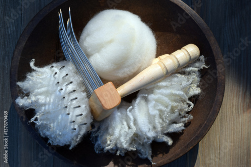 This is a bowl filled with natural sheep fleece locks, a fiber comb, and a nest of wool roving.