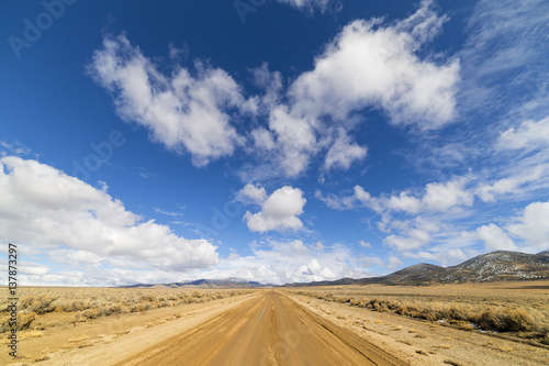 Dirt road in the Nevada desert under blue sky with clouds.  Road is wet dirt and mud.