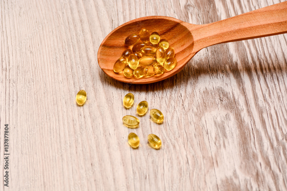 Vitamin D capsules in a wooden spoon on a wooden background, fish oil softgels, health and diet concept Vitamin D capsules in a wooden spoon on a wooden background, fish oil softgels, health and diet concept