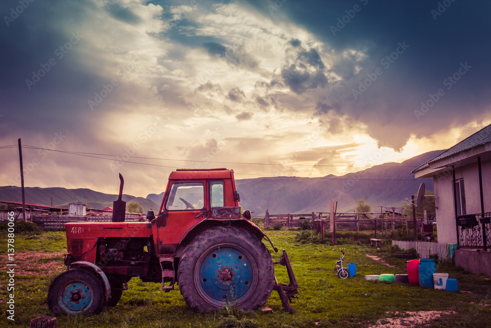 Fototapeta premium Very old tractor on the grass field and dramatic sky