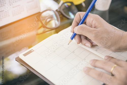 Close up of hands woman, writing something and daily appointment, meeting agenda, management on 2022 calendar book. On the desk have glasses calendar and notebook.