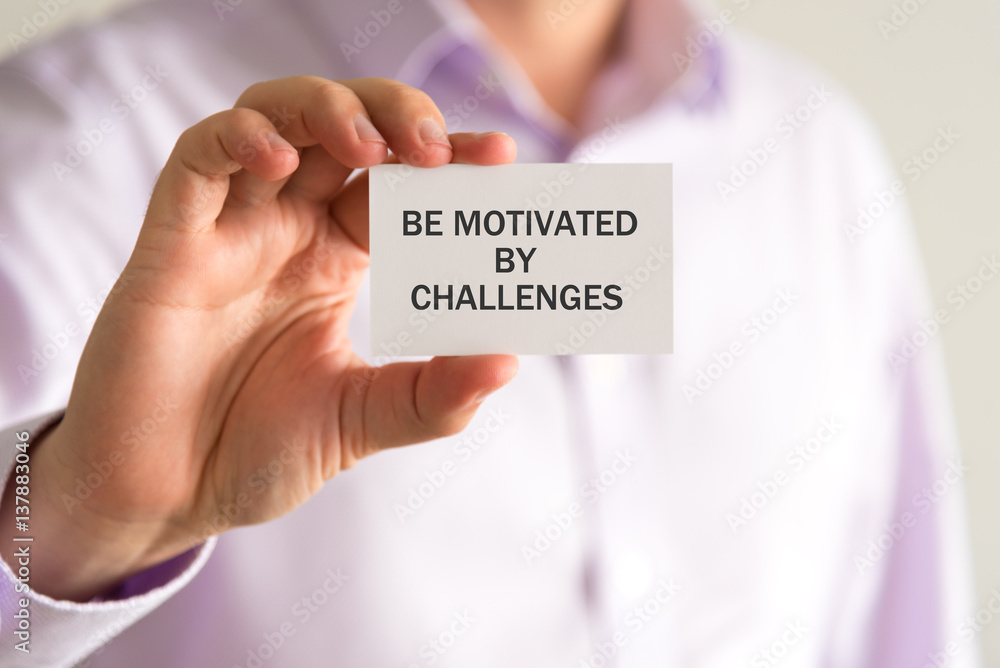 Businessman holding a card with text BE MOTIVATED BY CHALLENGES Businessman holding a card with text BE MOTIVATED BY CHALLENGES