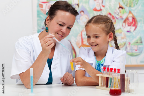 Teacher helping little girl student with elementary chemistry science experiment