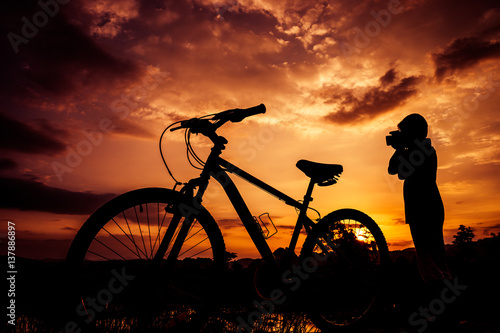 Silhouette of boy and bicycle on sunset background