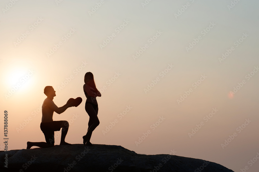 Lovely young adult couple standing on the rocks above tropical sea in Sunset.