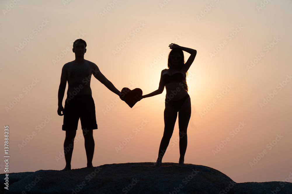 Lovely young adult couple standing on the rocks above tropical sea in Sunset.