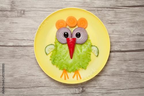 Funny chicken made of vegetables on plate and desk