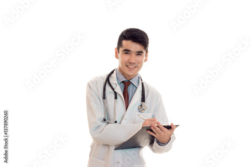 young perky doctor keeps a stethoscope on the shoulders and board in hand isolated on white background