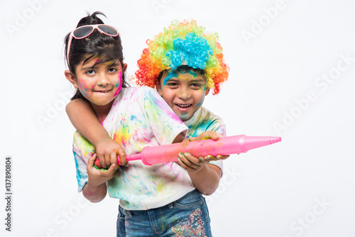 indian kids and holi festival with colourful faces playing colours with hand or pichkari or holding presenting something or holding sweets or laddu