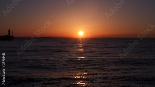 Seascape at dawn. We see the lighthouse and ship. In the sea swim seabirds