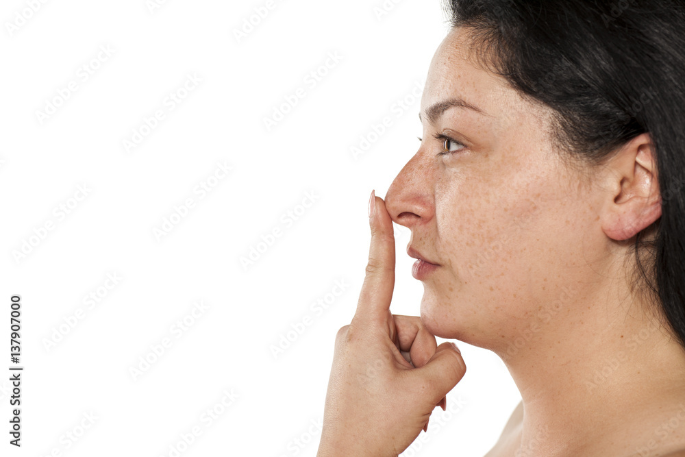 Profile of young smiling chubby and freckled woman without makeup touching her nose Profile of young smiling chubby and freckled woman without makeup touching her nose