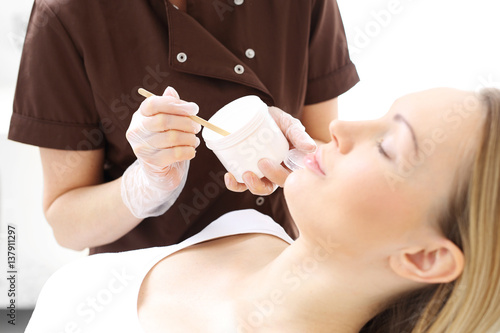 Maseczka kosmetyczna. Kobieta w salonie kosmetycznym, kosmetyczka nakłada pędzelkiem maseczkę na skórę twarzy.