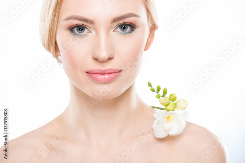Attractive blonde woman with white flower on shoulder smiling at camera  skincare concept