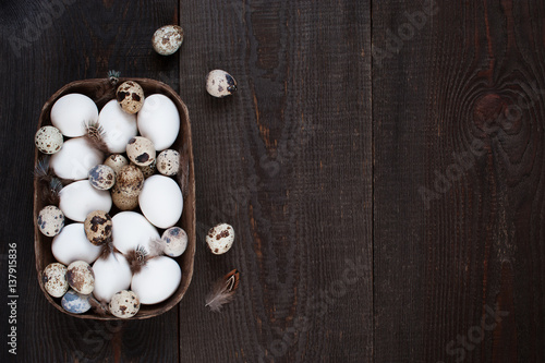 Wooden background with various fresh raw eggs and feathers