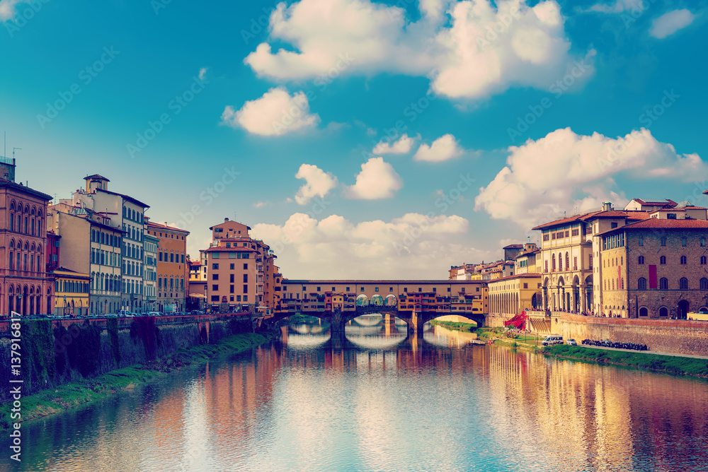 View from the river to the famous italian medieval bridge - Ponte Vecchio in Florence with blue sky and clouds, travel outdoor Italy sightseeing background