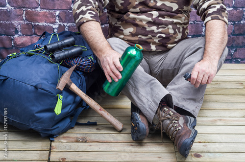 Close Up of One Person who wears boots for trekking and Mountain, with close Tools and Accessories as a compass, backpack, drinking bottle and ax Rock
