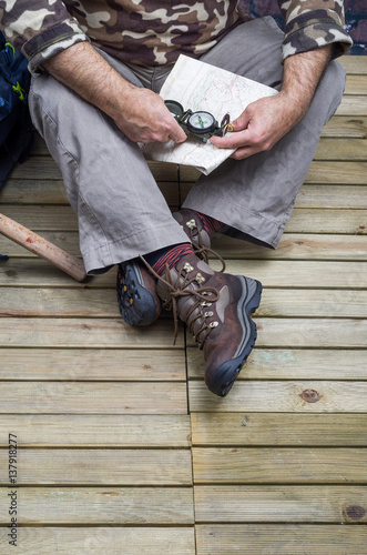 Close Up of One Person who wears boots for trekking and Mountain, with close Tools and Accessories as a compass, backpack, drinking bottle and ax Rock