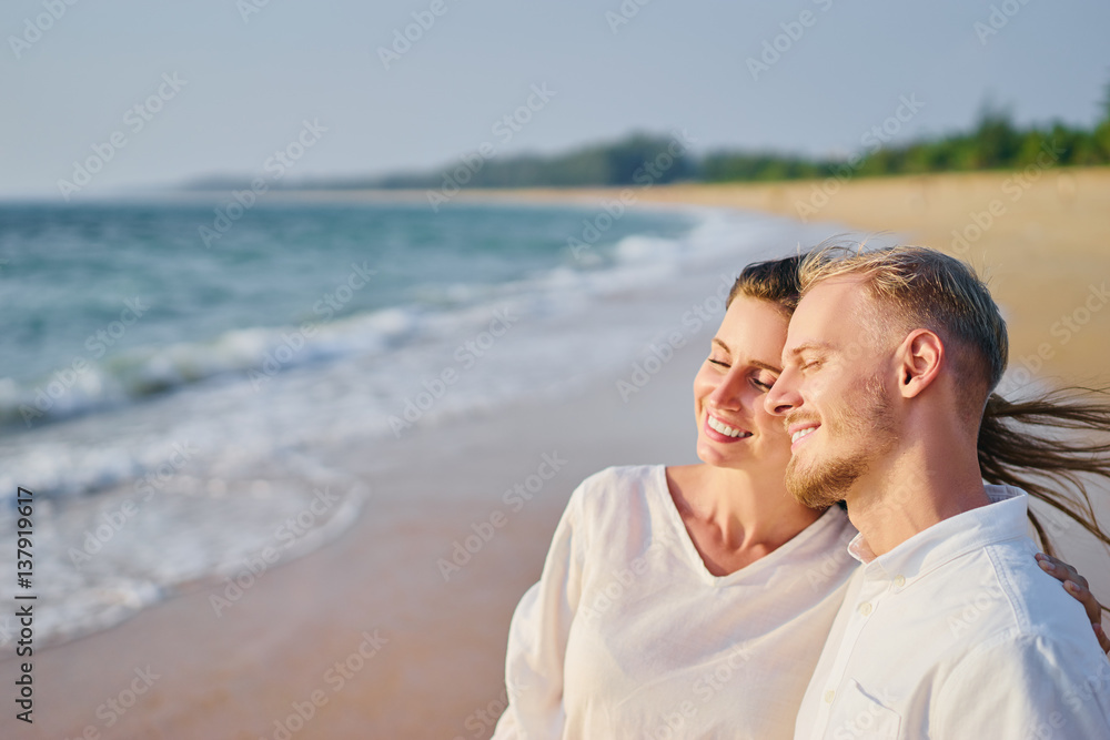 Love and romance. Honeymoon on the sea shore. Beautiful loving couple in white cloth on the beach.