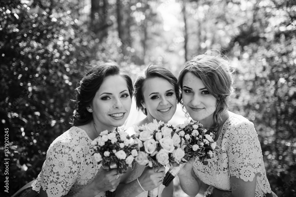 Bride with bridesmaids with wedding bouquet at hand on sunny forest. Black and white photo. Bride with bridesmaids with wedding bouquet at hand on sunny forest. Black and white photo.