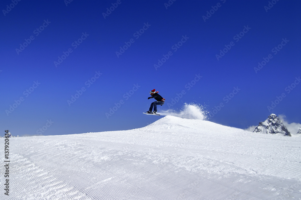 Snowboarder jumping in snow park at ski resort on sun winter day