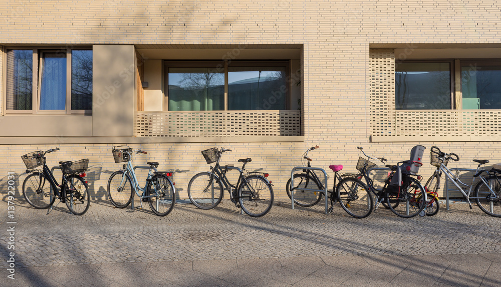 Variety of Bicycles Parked on Sidewalk in Front of Apartment Building, Sunny Weather