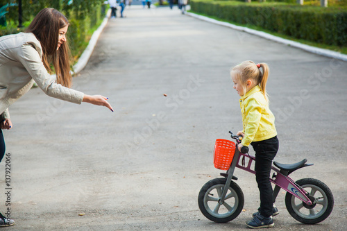 Young woman plays with little girl outdoors. Toddler on pushbike