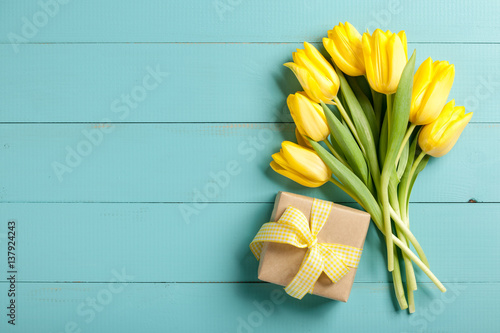 Yellow tulips and gift box on blue wooden background