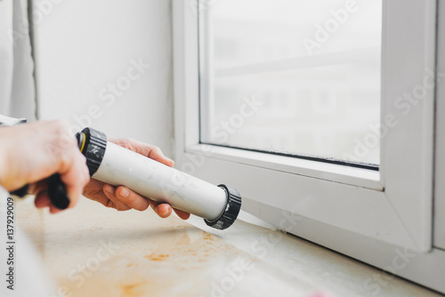 Hands of worker using a silicone tube  for repairing of window photo