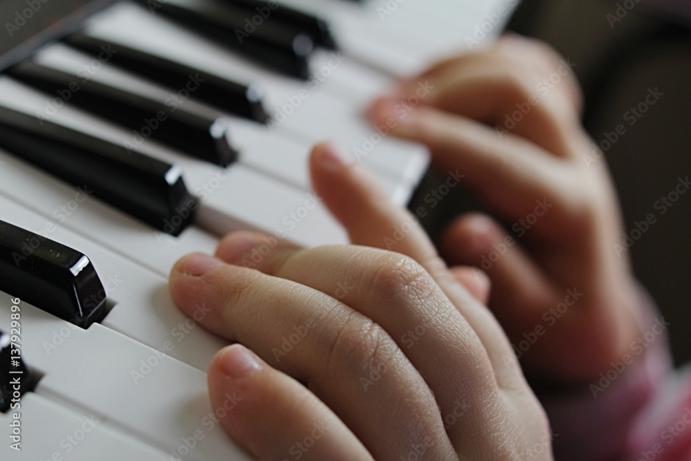 Fingers of small girl playing notes on miniature piano keyboard