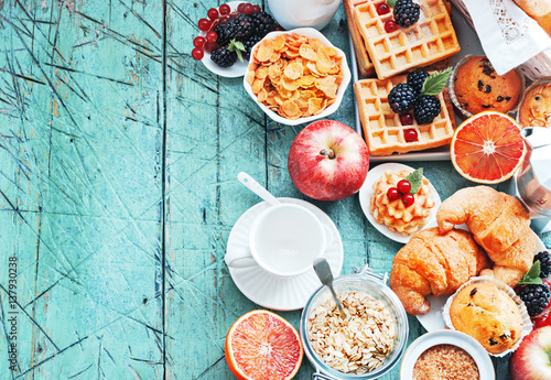 Healthy and colorful breakfast - cup of coffee with homemade granola, waffles, muffins,almond,hazelnuts,various fresh fruits, berries and milk on old wooden table.