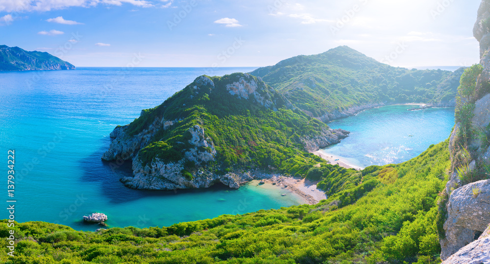 Beautiful summertime panoramic seascape. View of the cliff into the crystal clear azure sea bay and distant islands. Unique secluded beach. Agios Stefanos cape. Afionas. Corfu. Greece. Beautiful summertime panoramic seascape. View of the cliff into the crystal clear azure sea bay and distant islands. Unique secluded beach. Agios Stefanos cape. Afionas. Corfu. Greece.