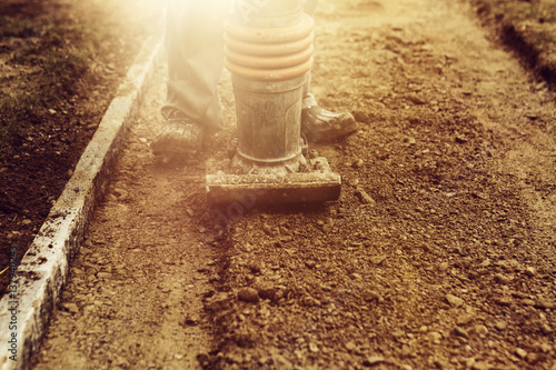 Stamping soil with rammer to build the garden path in the evening sunshine